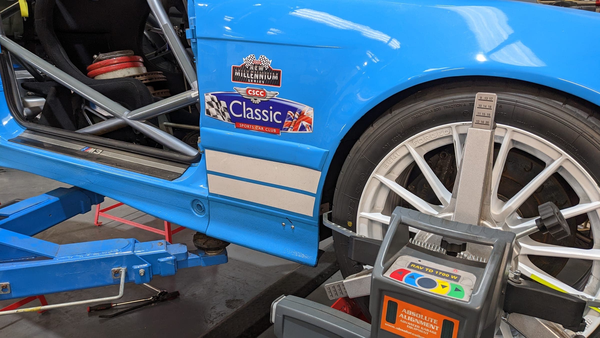 A blue E36 race car on an alignment rig, with a sensor on the wheel