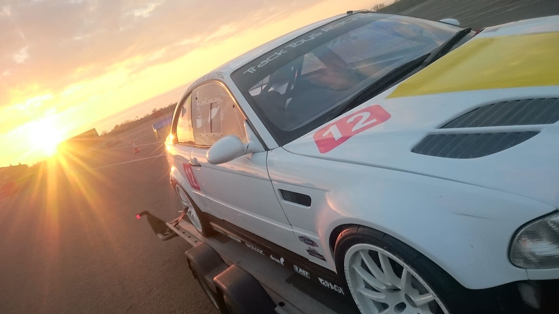 A white BMW race car on track at sunset